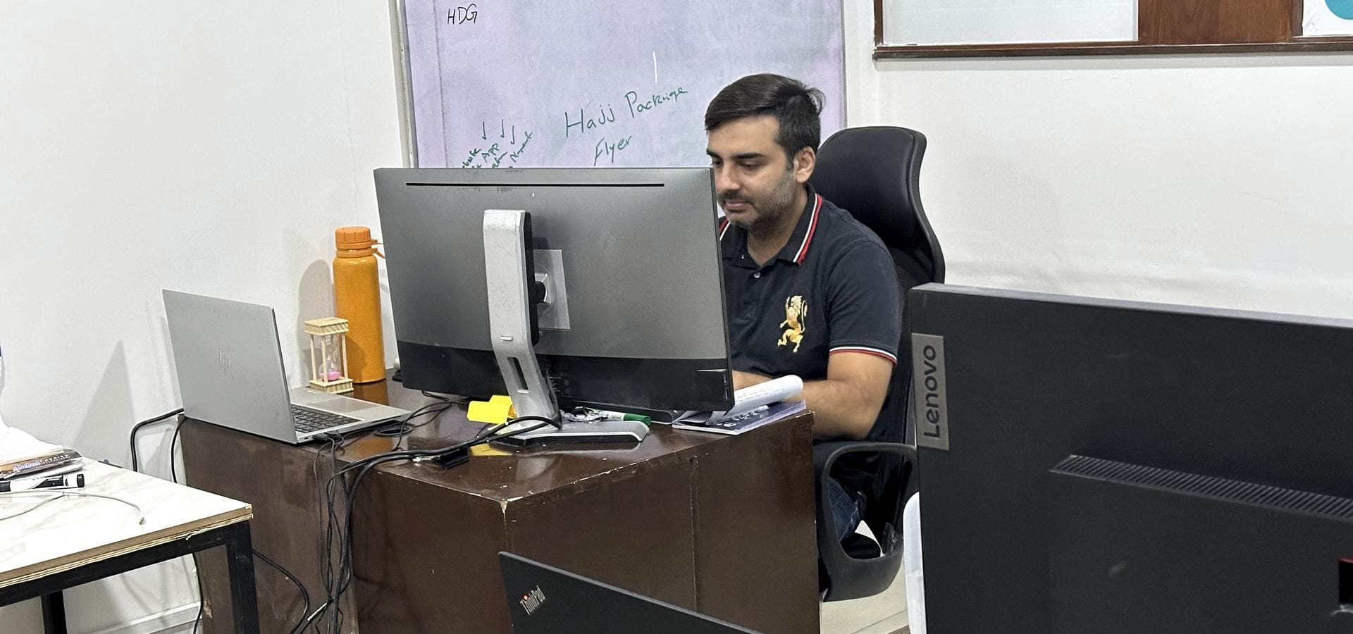 Someone at a desk in the 02X room in Faisalabad, whiteboard behind them.