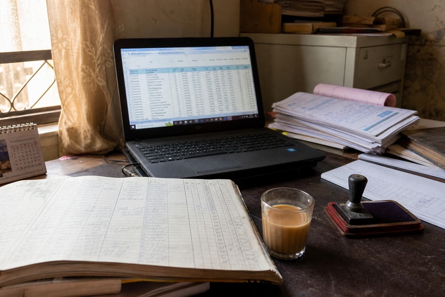 A desk with a ledger, invoices and a laptop — the job a system is meant to take.