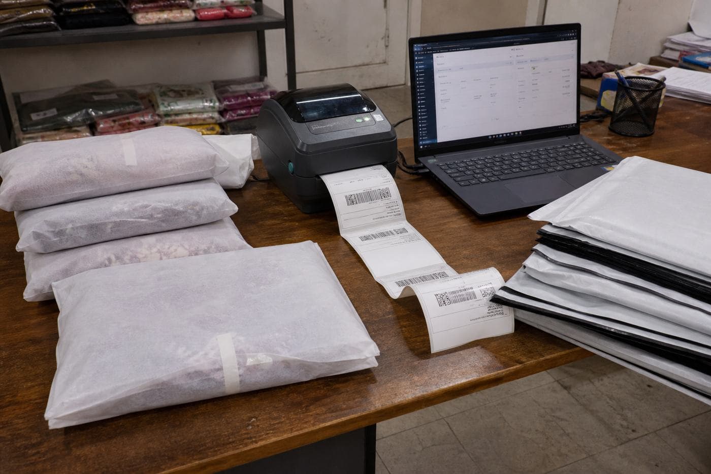 Packing table with lawn suits, mailers and an orders laptop.